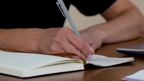 Close-up of a person writing notes in a diary or planning book at home office Stock Footage 323167033