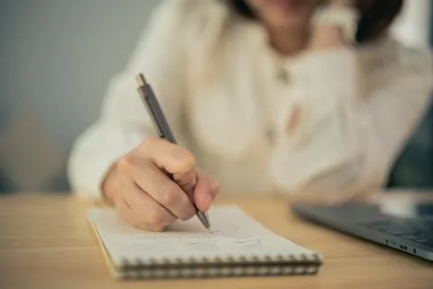Close-up of person writing notes with pen on notebook at wooden desk Stock Photos