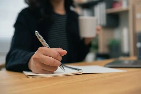 Close-up of person writing notes with pen in notebook while holding cup in .. Stock Photos