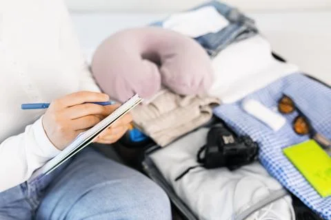 Close-up of a person writing a packing list in a notebook next to an open s.. Stock Photos