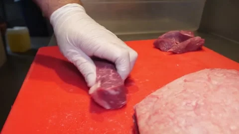 Close-up of a person's hand cutting raw red meat on a red cutting board 스톡 동영상 332811889