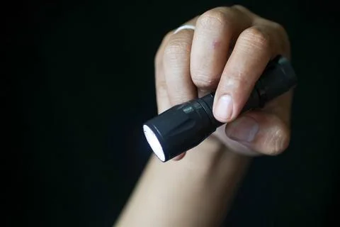Close-up of a person's hand holding a flashlight on a black background. Stock Photos
