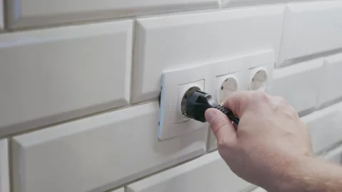 A close-up of a person’s hand inserting a black power plug into a white Stock Footage 320563004