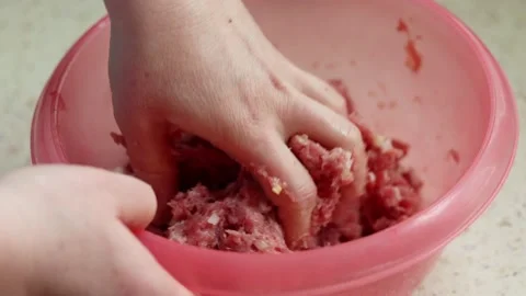 Close-up of a person's hand kneading raw minced meat in a red plastic bowl. Video stock 239014986
