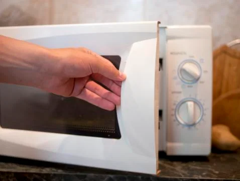 Close up person's hand opens microwave oven to heat some fried food Foto stock