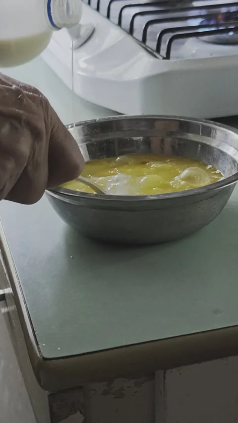 Close up of a person's hand pouring milk into a steel bowl with beaten eggs Stockbeeldmateriaal 342608492