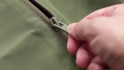 Close-up of a person's hand pulling the zipper slider on a green fabric jacket. Stock-Footage 344583092