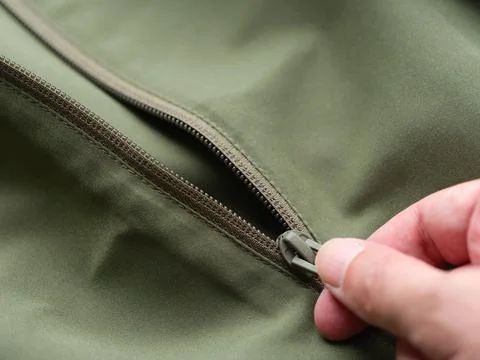 Close-up of a person's hand pulling the zipper slider on a green jacket Stock Photos