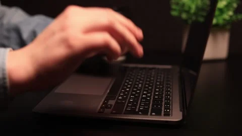Close-up of a person's hand reaching for a laptop keyboard in a dimly lit Stock Footage 338432528