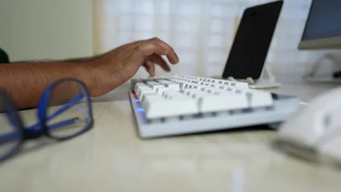 Close-up of a person's hand typing on a white keyboard with glasses nearby Stock Footage 317737123