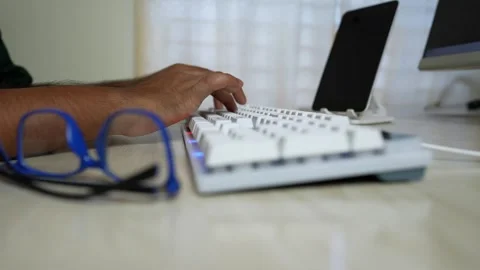 Close-up of a person's hand typing on a white keyboard with glasses nearby Stock Footage 317737126