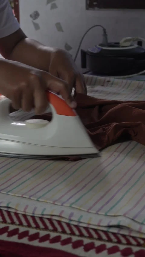 Close-up of a person's hand using a modern white and orange electric steam iron  動画素材 337869850