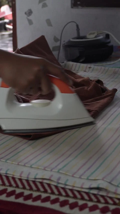Close-up of a person's hand using a modern white and orange electric steam iron  Video stock 337870004
