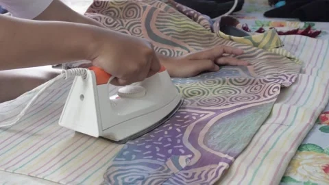 Close-up of a person's hand using a modern white and orange electric steam iron  Video stock 337870129