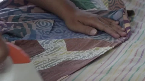 Close-up of a person's hand using a modern white and orange electric steam iron  動画素材 337870240