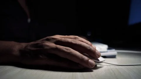 Close-up of a persons hand using a white computer mouse on a desk in a dark.. Vidéo 334285796