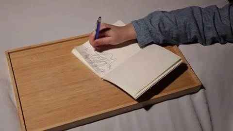 Close-up of a person's hand writing in a notebook on a wooden tray Stock Footage 339177570