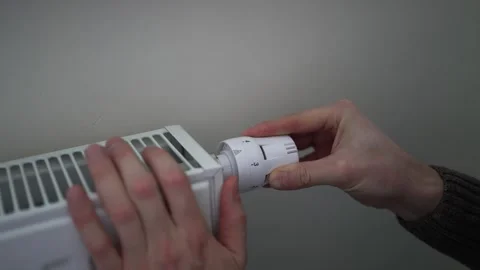 Close-up of a person's hands turning the thermostat dial on a white heating Stock Footage 323388744