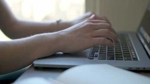 A close-up of a persons hands typing on a laptop keyboard at a wooden desk by a 스톡 동영상 280007171