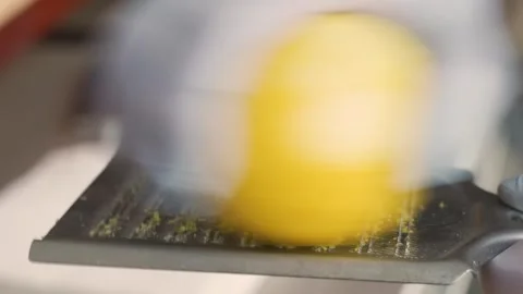 Close up of a person's hands wearing gloves grating fresh yellow lemon zest with Stock Footage 333600533