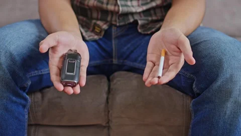 Close-up of person's hands weighing options of vape device versus conventional Stock Footage 332477655