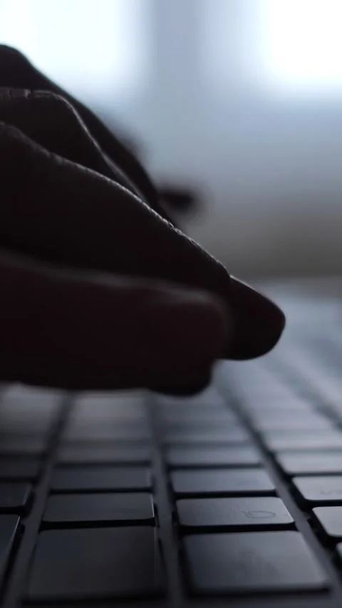 Close up of a persons silhouetted fingers typing quickly on a dark laptop Stock Footage 344798557