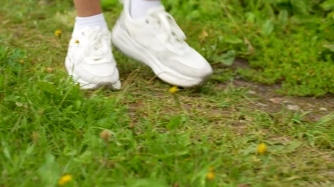 Close-up of a person's white sneakers walking firmly on green grass and dir.. Stock-Footage 314006201