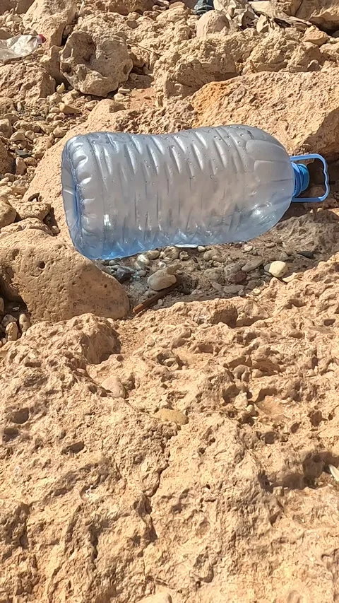 A Close-Up Perspective on a Clear Plastic Water Bottle Resting Amongst Rocky 库存影片 330096955
