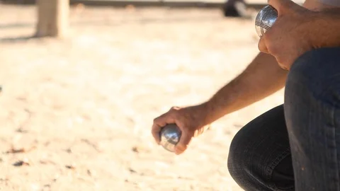 Close up of a petanque player holding 2 metal balls in his hand and shooting Видео 110764935