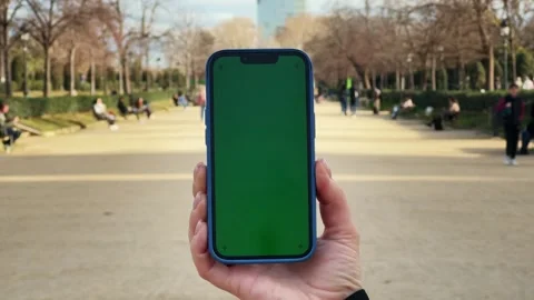 Close up of phone with vertical green screen in hands on city park background Stock Footage 284446068