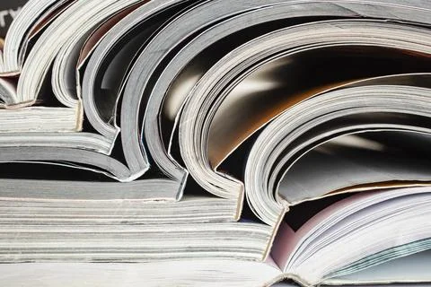 Close-up photograph of a stack of open magazines or journals, abstract text.. 스톡 사진