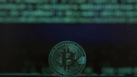 Close-up: physical Bitcoin coin, with a blurred green digital rain code falling Stock Footage 332591066