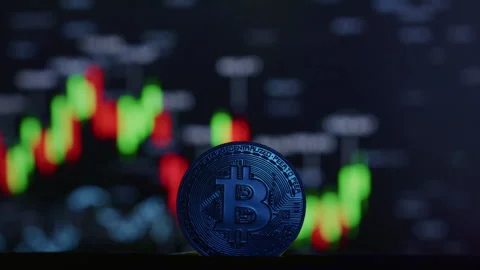 Close-up: physical Bitcoin coin, blurred cryptocurrency exchange chart, showing Stock Footage 332621413