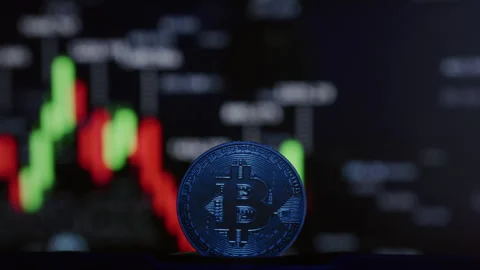 Close-up: physical Bitcoin coin, blurred cryptocurrency exchange chart, showing Stock Footage 332621984