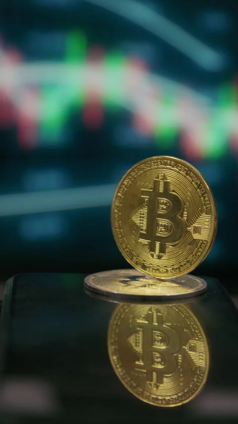 Close-up of a physical Bitcoin with an out-of-focus crypto trading chart Stock Footage 334771331