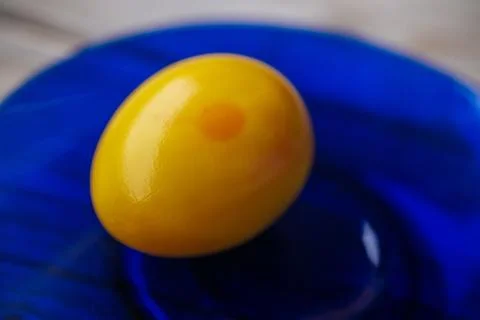 A close-up of a pickled egg with a smooth, shiny yellow surface. Photos