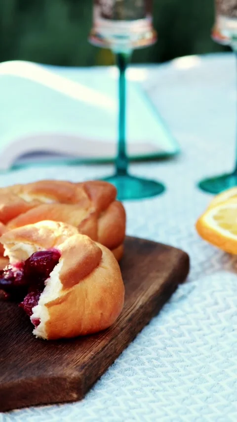 Close-up picnic table scene with torn berry bun showing dark jam, whole golden Stock Footage 345161790