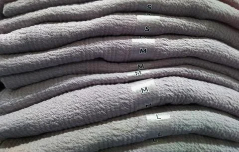 Close up pile of gray sweaters with size description (S,M,L). Stock Photos