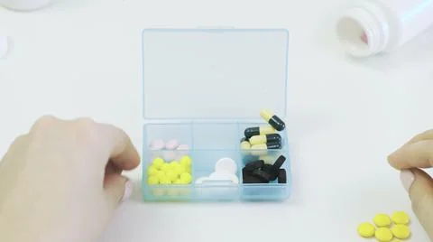 Close-up of a pillbox with different tablets. A person's hands put pills in a 写真素材
