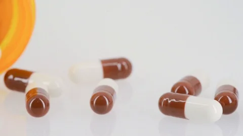 Close up of pills spilling out of pill bottle - slow pan - white background Stock Footage 104530446