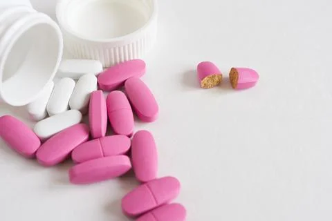Close-up of pink and white tablets on white background with space for copying. Stock Photos
