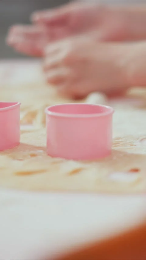 Close up pink plastic cookie cutters resting on rolled out raw dough with hands Stock Footage 345987532