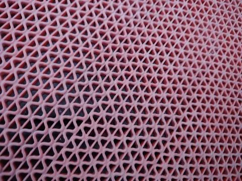 Close-up of a pink plastic mesh grid showing repeating triangular openings .. Stock Photos