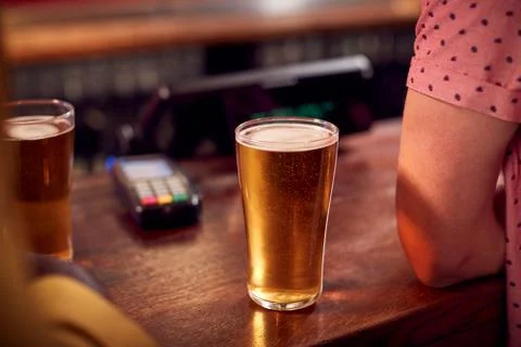 Close Up Of Pints Of Beer Standing On Counter Of Bar With Customer Stock Photos