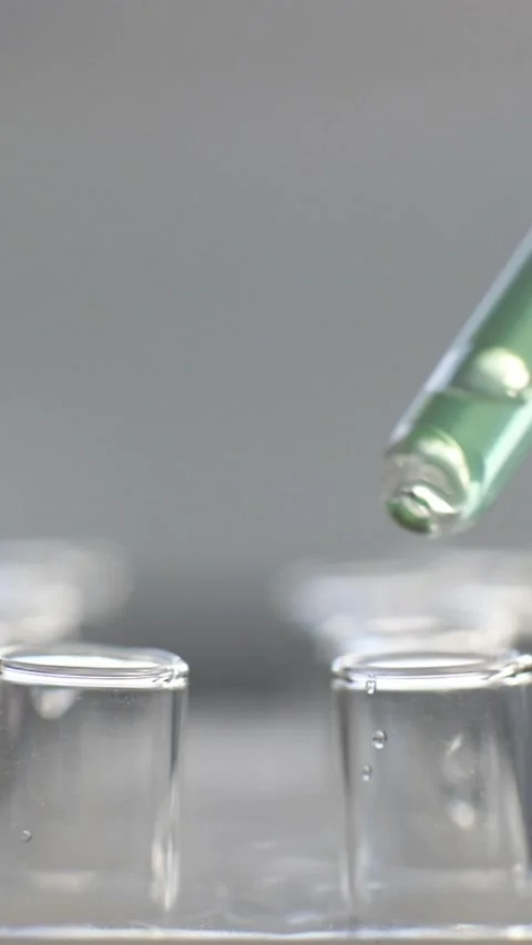 Close-up of a pipette dripping clear liquid into a laboratory test tube during a Stock Footage 335521784