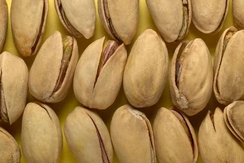 Close-up of pistachio nuts in their shells arranged in a pattern on a yellow Stock Photos