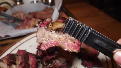 Close up of pitmaster using metal tongs to lift a juicy slice of smoked beef bri 스톡 동영상 332814200