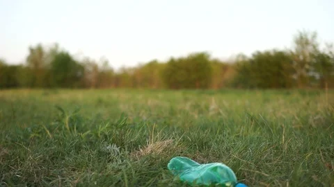 Close plan the hand of a volunteer picks up a plastic bottle from the grass in Stock Footage 107603816
