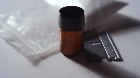 Close-up of a plastic bag, a razor, and a jar of cocaine spinning on white Video stock 119094321