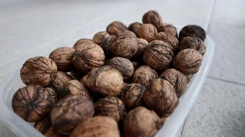 A close-up of a plastic container filled with whole walnuts. Stock Photos